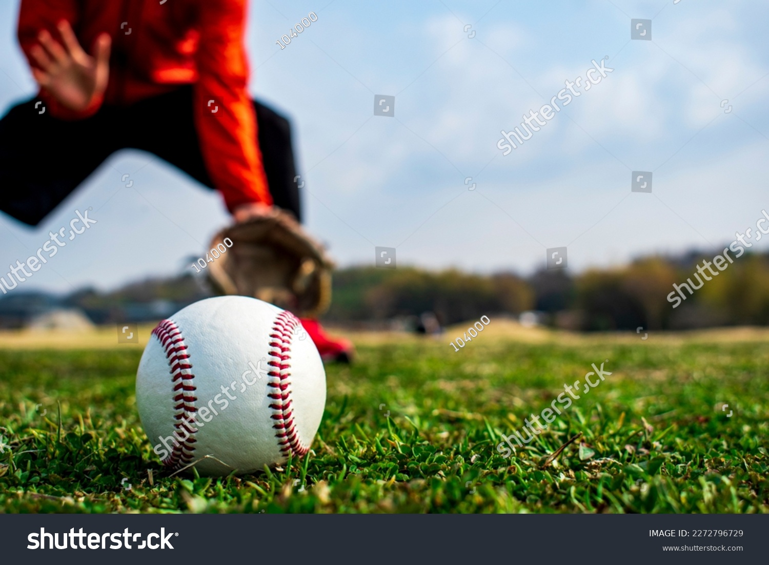Baseball ball on the lawn. Man in catching position in background. #2272796729