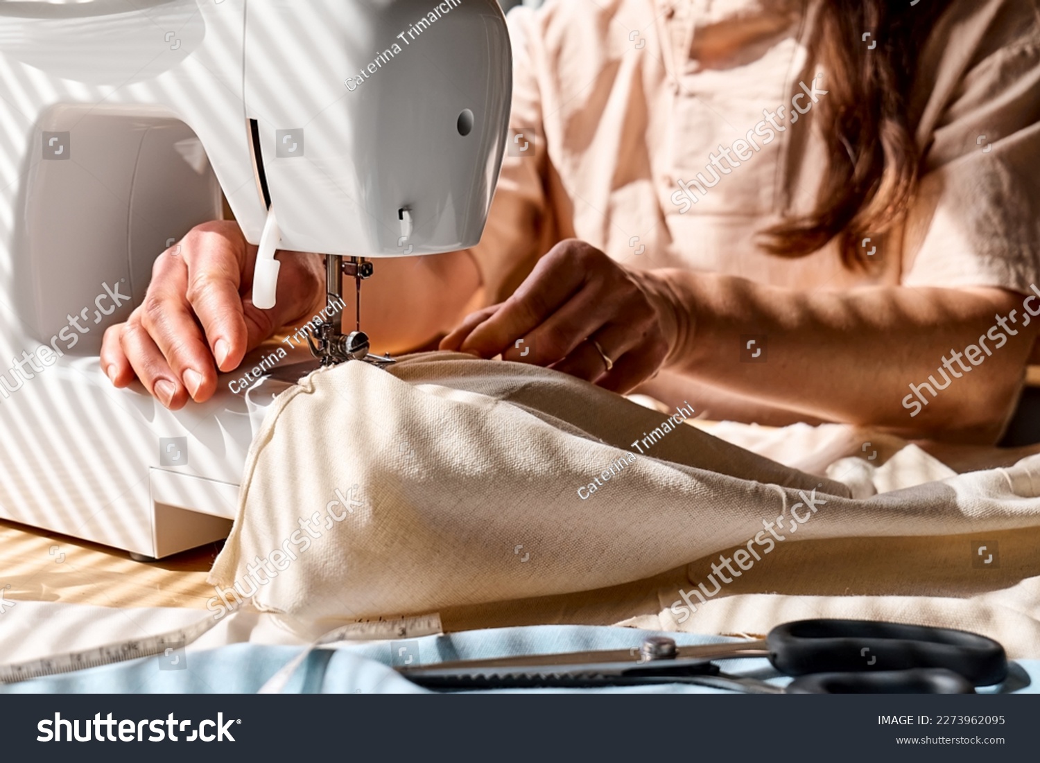 Seamstress sewing linen fabric on sewing machine in small studio. Fashion atelier, tailoring, handmade clothes concept. Slow Fashion. Conscious consumption. #2273962095