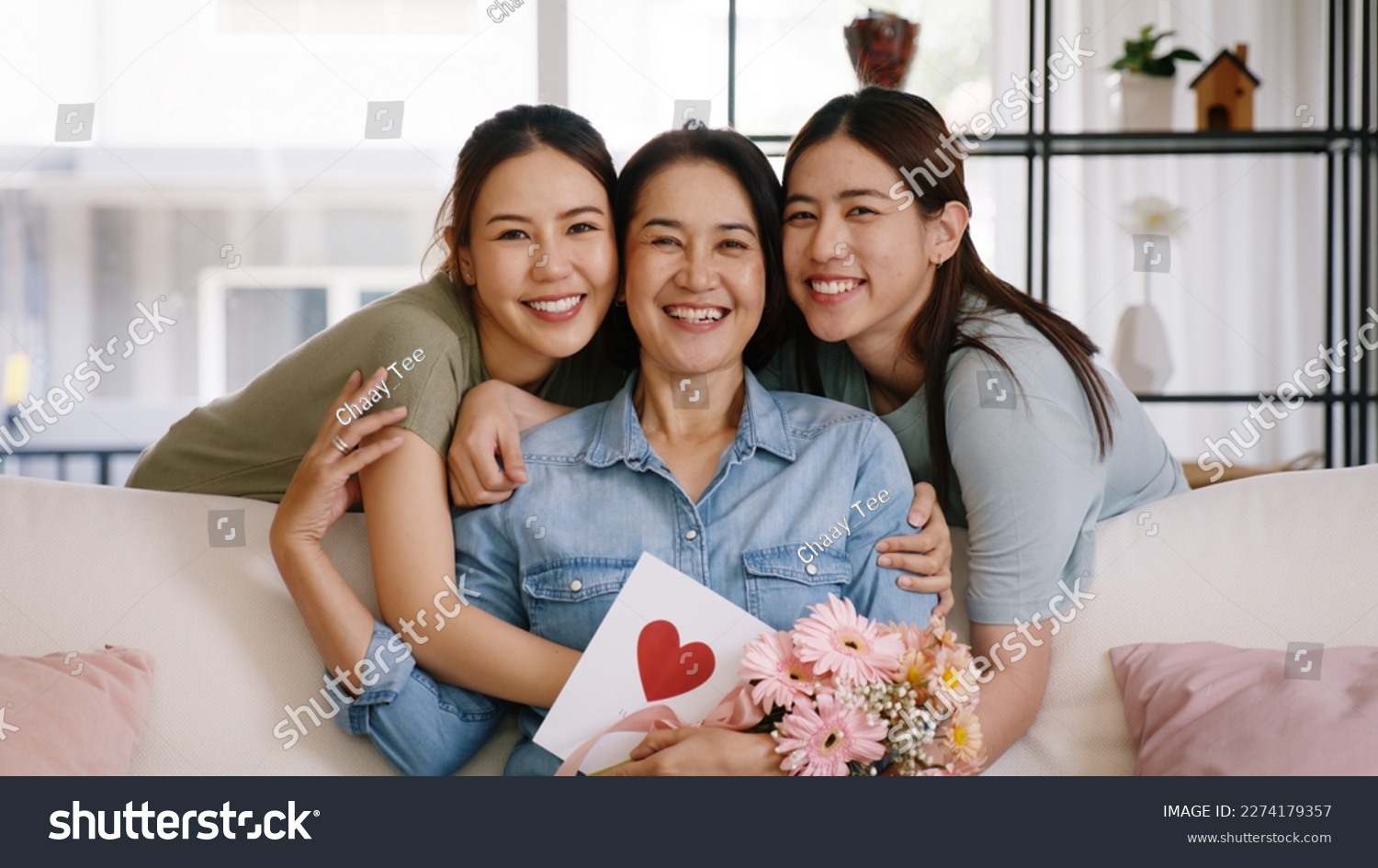 Happy time Mother day grown up child looking at camera cuddle hug give flower gift box red heart card to mature mum. Love kiss care mom asia middle age adult people smile enjoy sitting at home sofa. #2274179357