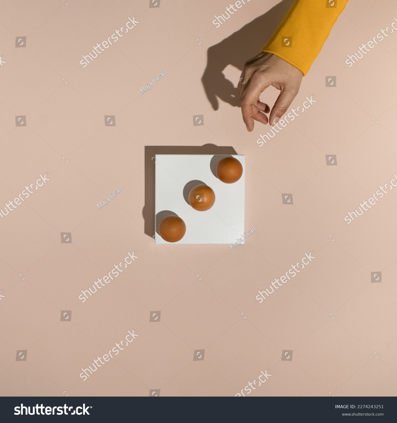 Female hand reaching for three fresh brown chicken eggs on white rectangle stand. Minimal food concept. Flat lay. #2274243251