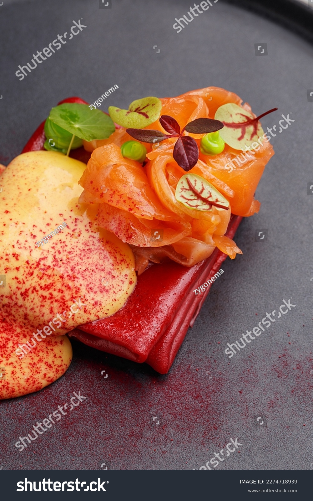 Colorful red crepes or blini with salmon and hollandaise sauce, decorated with micro greens on black plate. Gourmet snack. Fine dining. Close up view #2274718939
