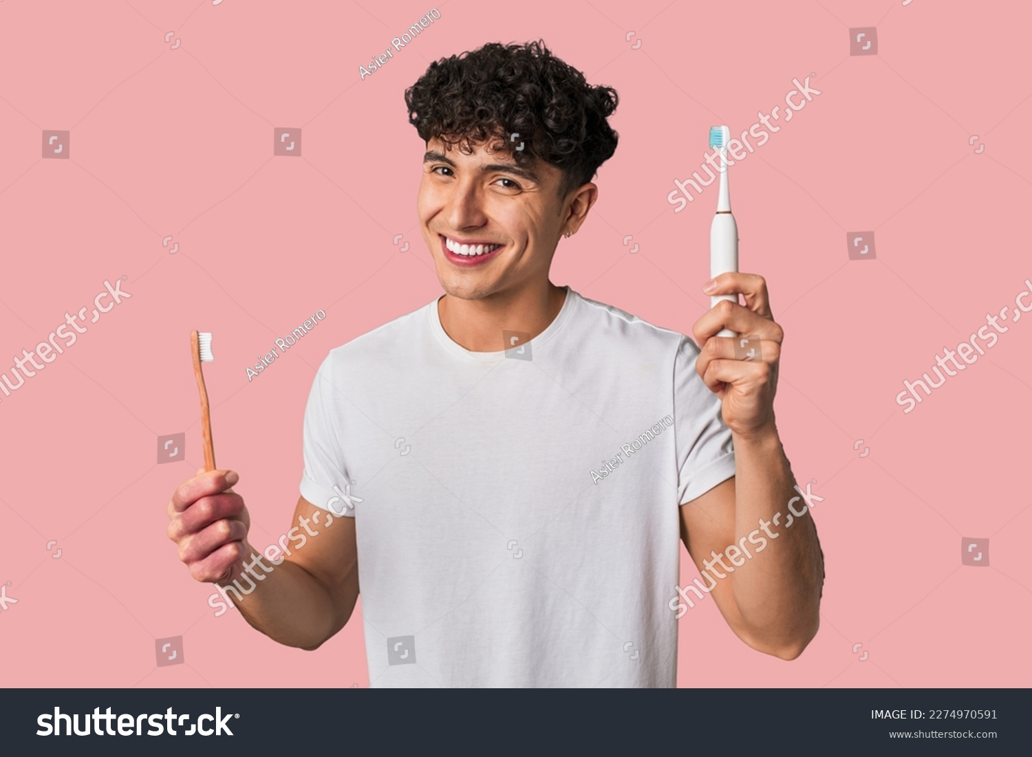 A young man compares manual vs electric toothbrush for optimal dental care - weighing effectiveness, convenience, and cost. #2274970591