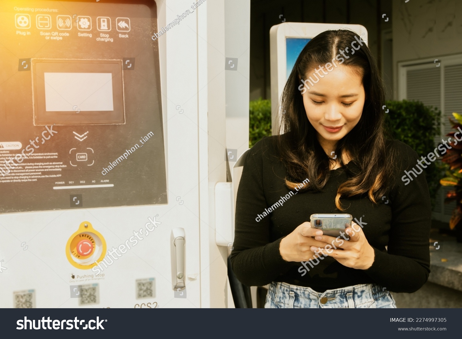 Young asian woman driving an EV electric vehicle using app to find convenient gas station charging an electric car and using scanned barcode to connect to the car to charge DC power to the battery
 #2274997305