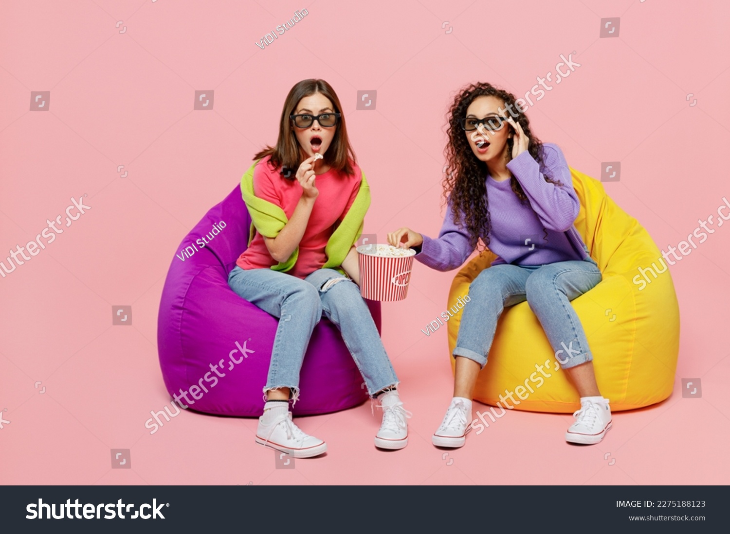 Full size young two friends shocked surprised amazed astonished women in 3d glasses watching movie film in cinema sit in bag chair isolated on pastel plain light pink color background studio portrait #2275188123