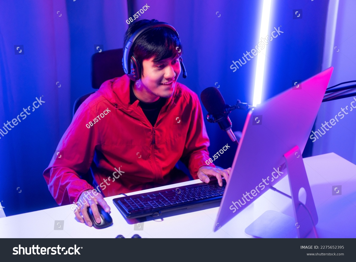 Professional gamer casting podcast walkthrough review. Young asian man sitting on chair with computer pc and microphone. Happy male Streamer wearing headphone playing game online in room neon light #2275652395