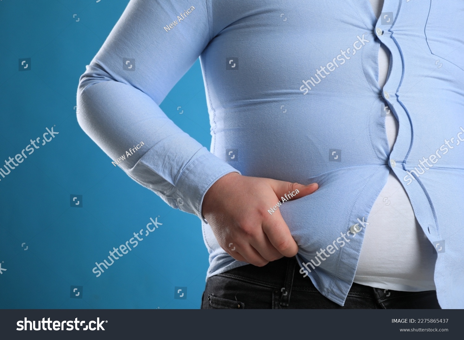 Overweight man in tight shirt on light blue background, closeup #2275865437
