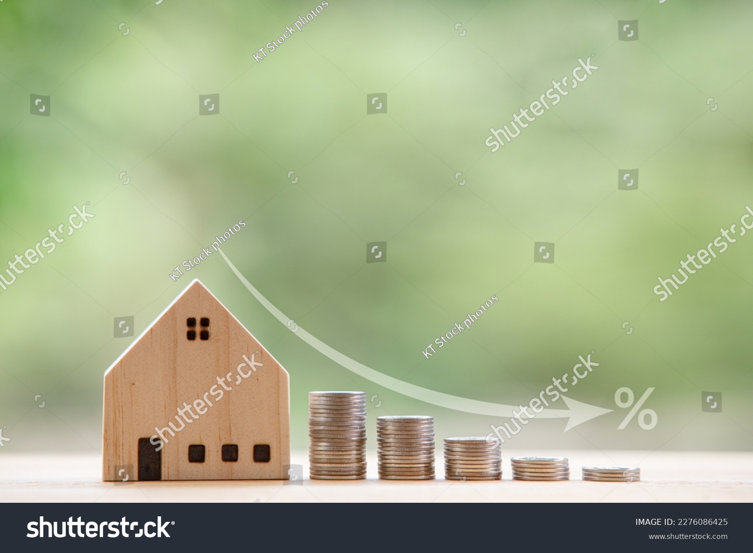 Model wooden house in front of a natural green backdrop and an arrow showing a falling rate of interest. Strategic ideas to get lower interest rates when buying and mortgage a home. #2276086425
