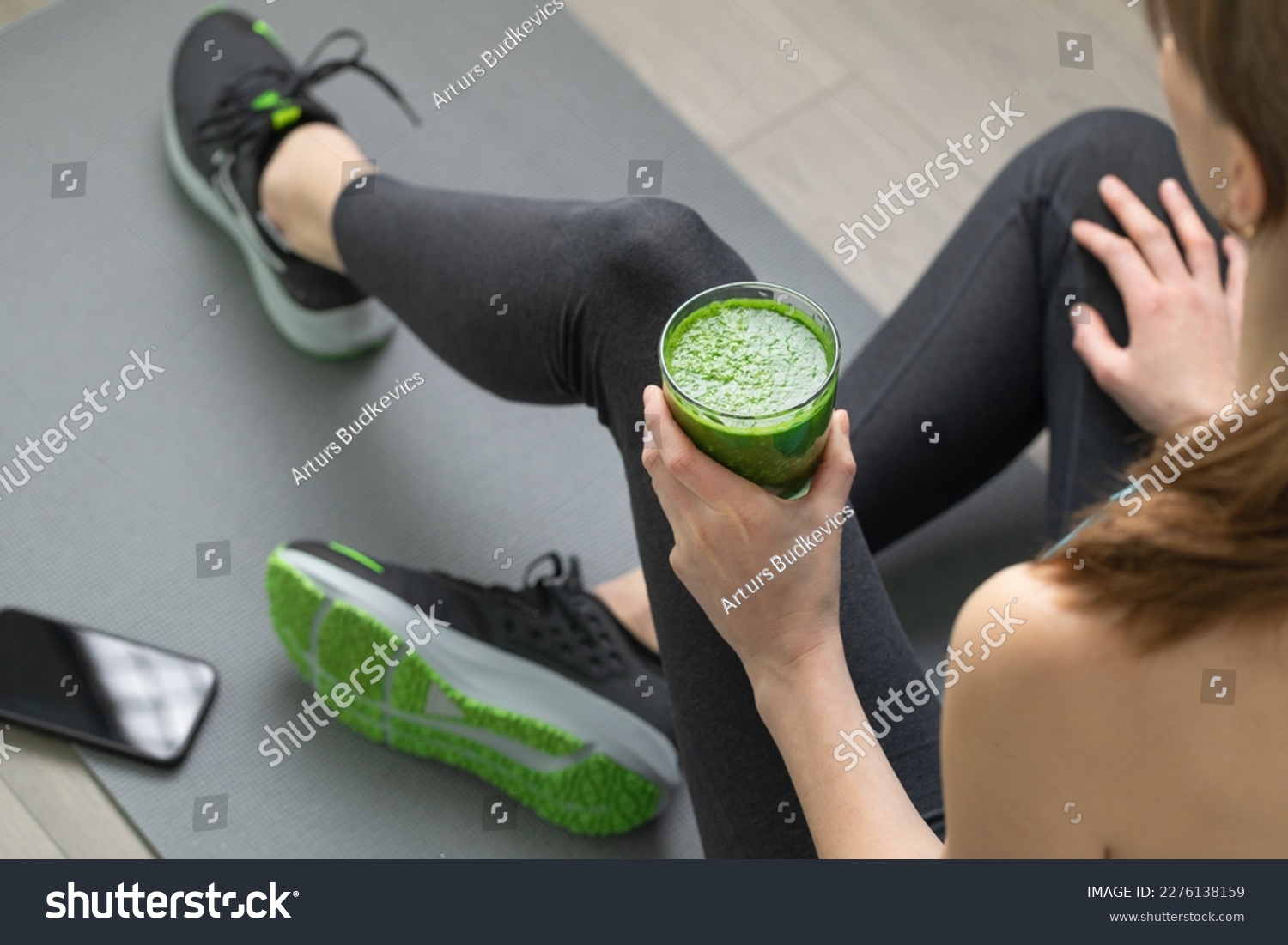 Women's hands tying sport shoes on a gray workout mat. With smoothie for detox in background. Healthy living, dieting lifestyle. #2276138159