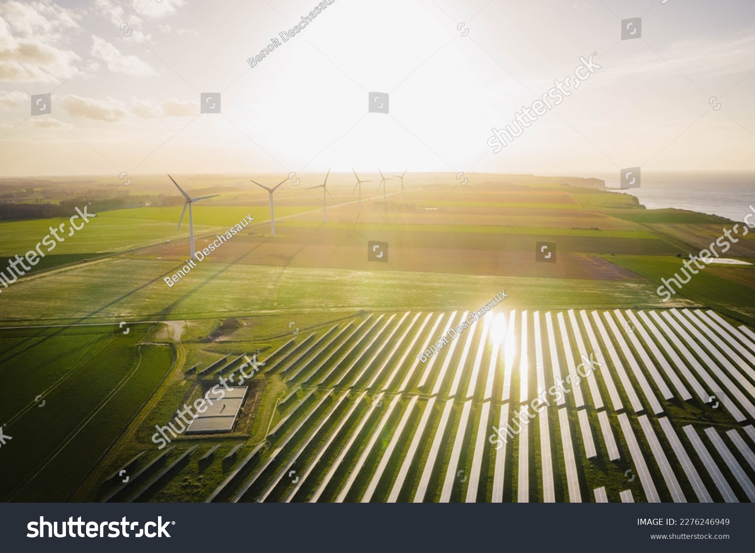 Windmills and solar panels farm in green fields close to the ocean. Renewable energies concept. Green energy for carbon dioxide emission reduction.  #2276246949