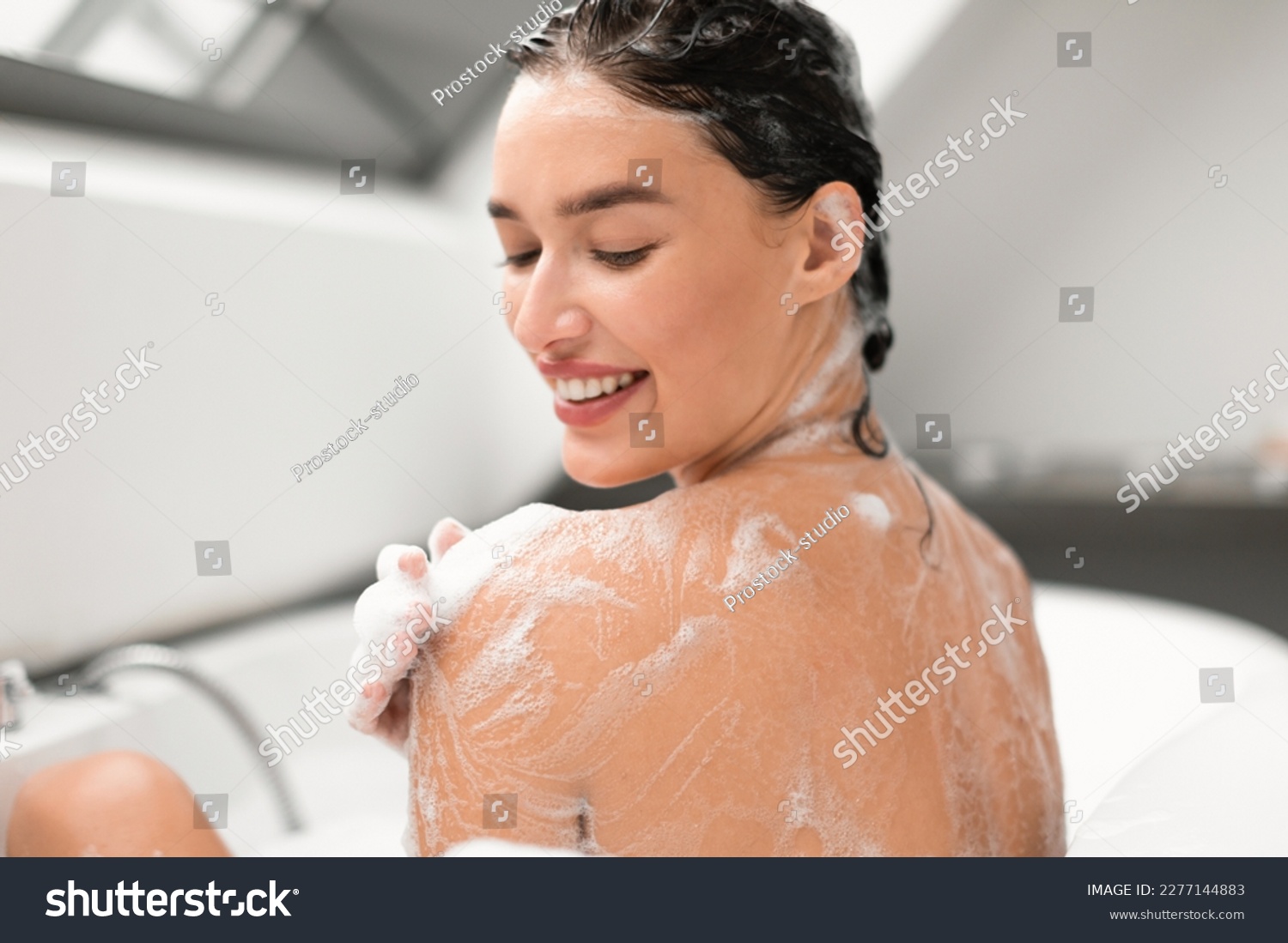 Pretty Woman Washing Body Taking Bath With Foam Applying Shower Gel On Shoulder Sitting Back To Camera In Bathtub In Modern Bathroom Indoors. Bodycare Beauty Routine Concept. Selective Focus #2277144883