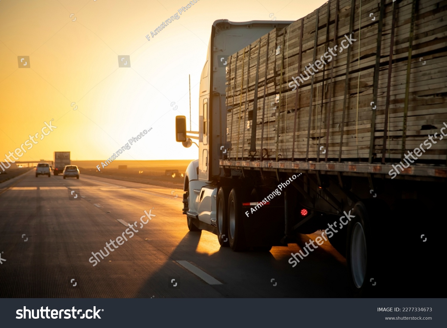 Long Haul 18 Wheel Truck driving on a highway with a load of lumber at sunrise or sunset  #2277334673