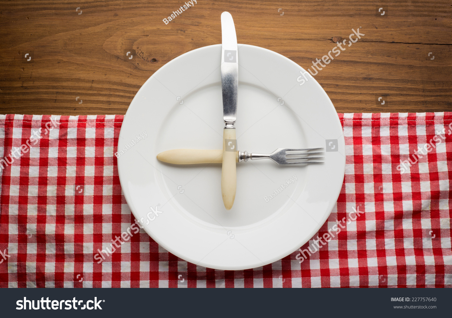 Empty plate with fork and knife on tablecloth over wooden background #227757640