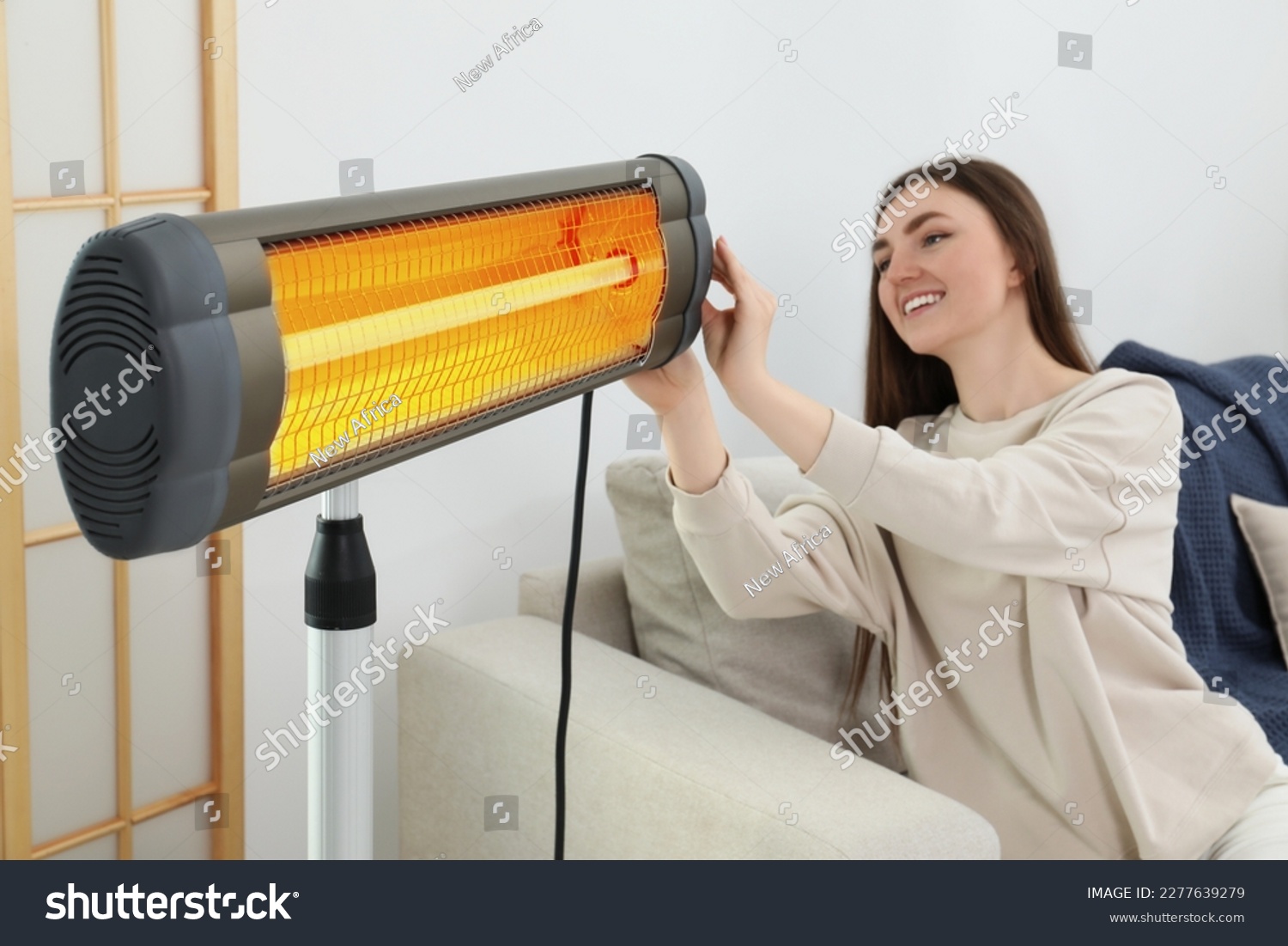 Woman adjusting temperature on electric infrared heater indoors #2277639279