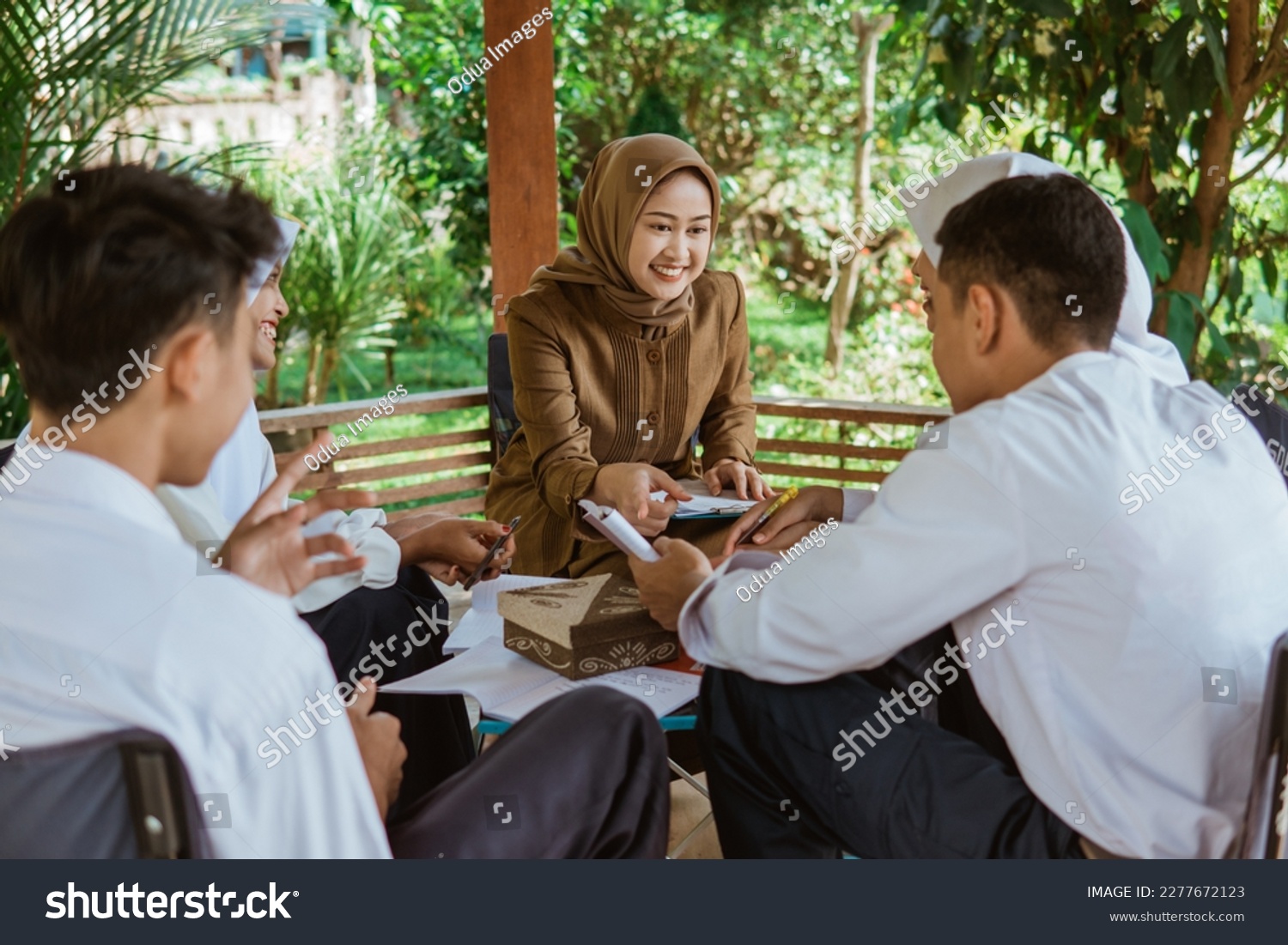 teacher in Veil guides students to do the questions in the book in the gazebo during outdoor class #2277672123