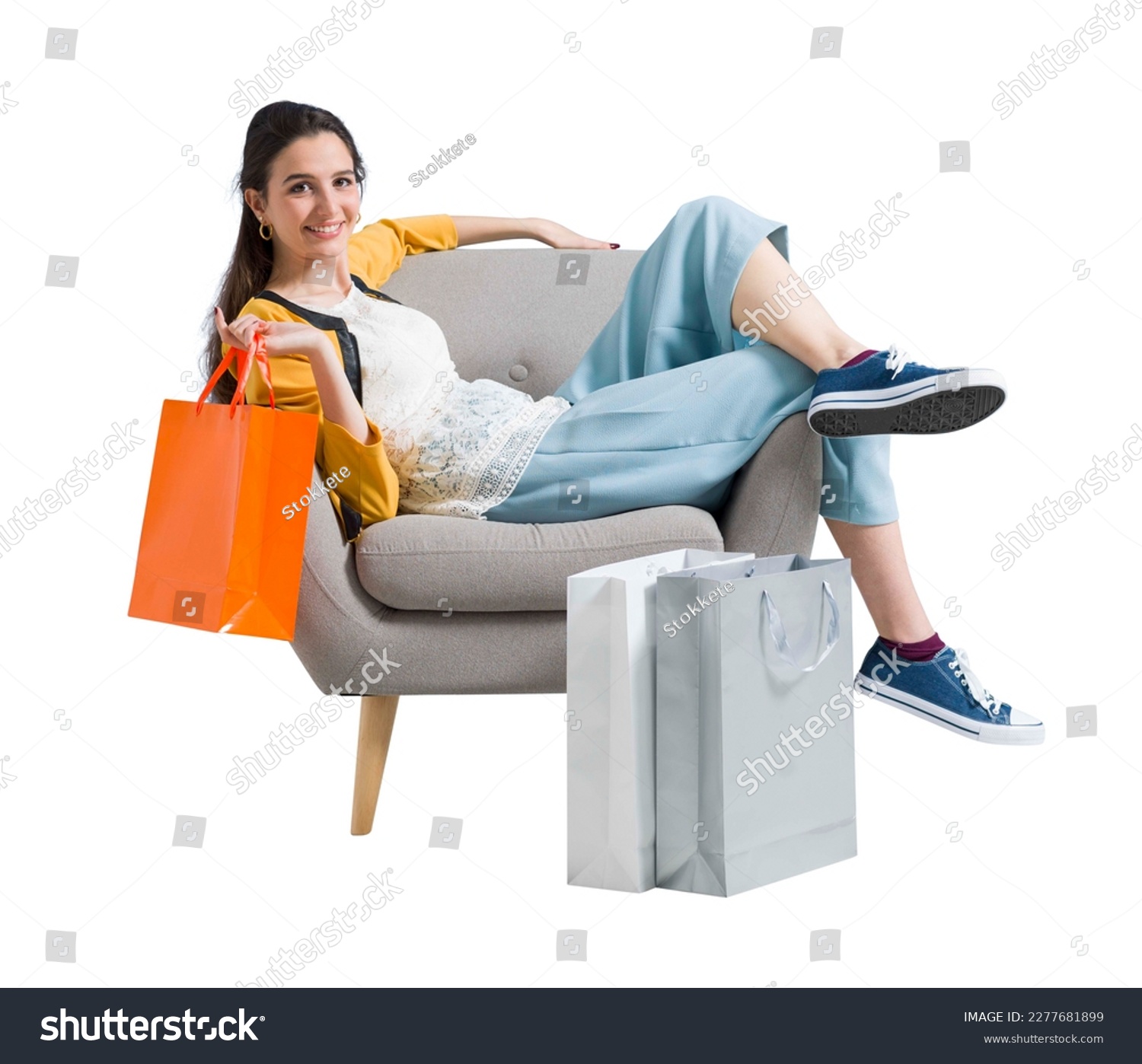 Cheerful happy shopaholic woman with lots of shopping bags, she is sitting on an armchair and celebrating with arms raised #2277681899