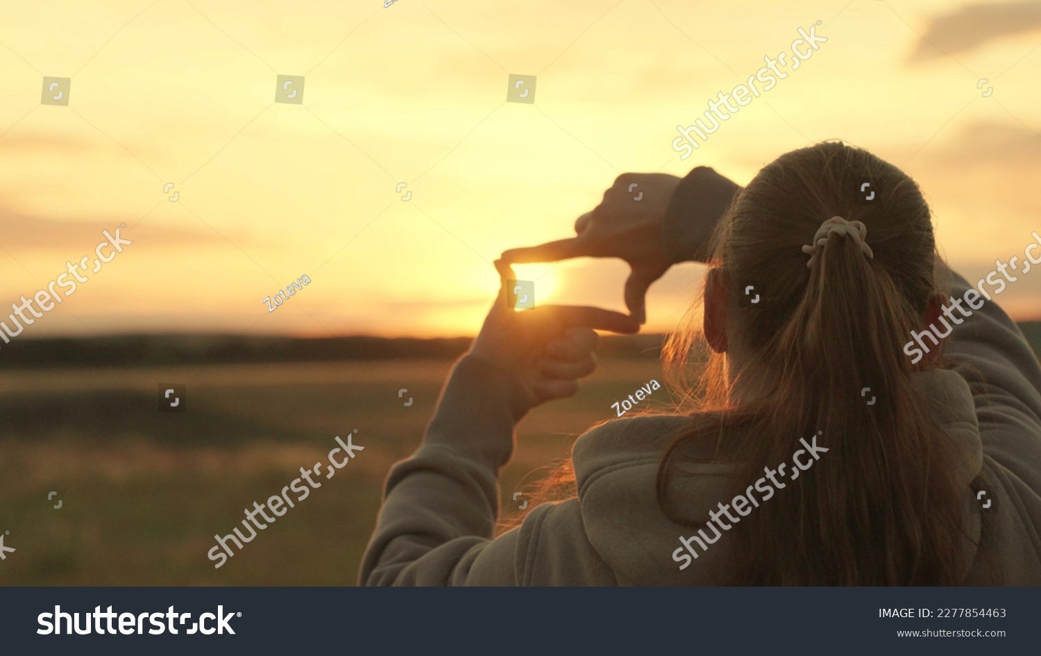 Girl shows her fingers frame symbol, sun. Hands of young female director cameraman making frame gesture at sunset in park. Sees like in movies. Concept of seeing world as different. Business planning #2277854463