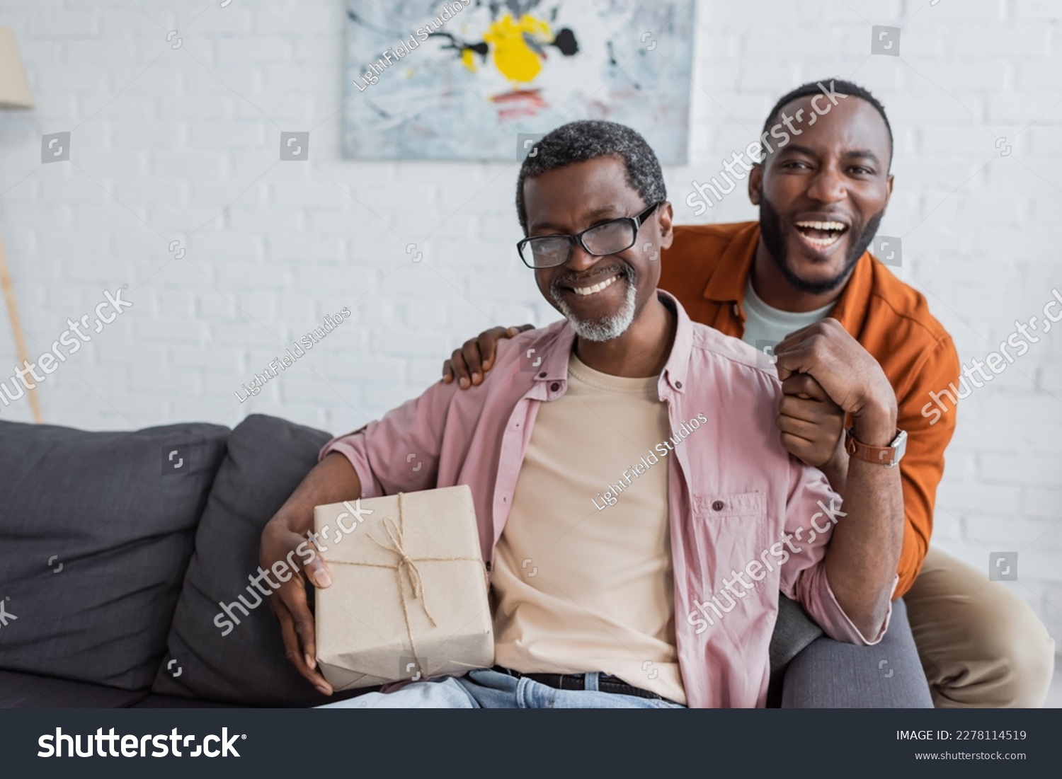 Cheerful african american middle aged man holding gift near son during father day celebration at home #2278114519