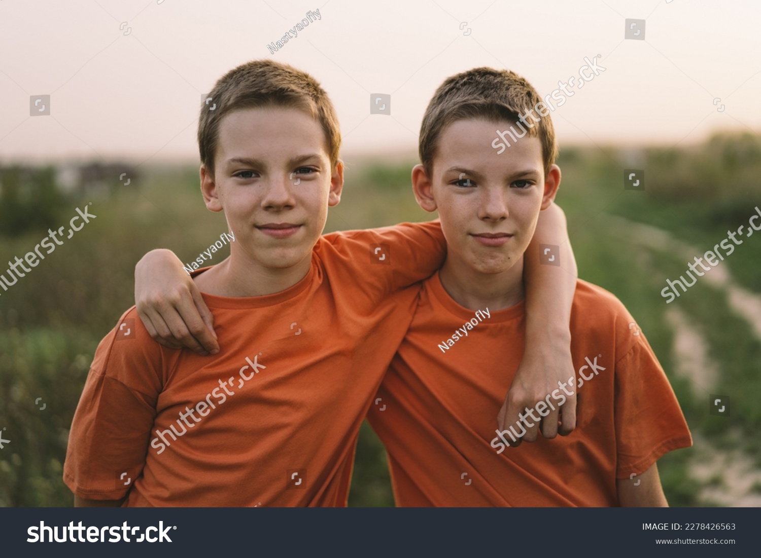 Funny twin brother boys in orange t-shirt playing outdoors on field at sunset. Happy children, lifestyle. #2278426563