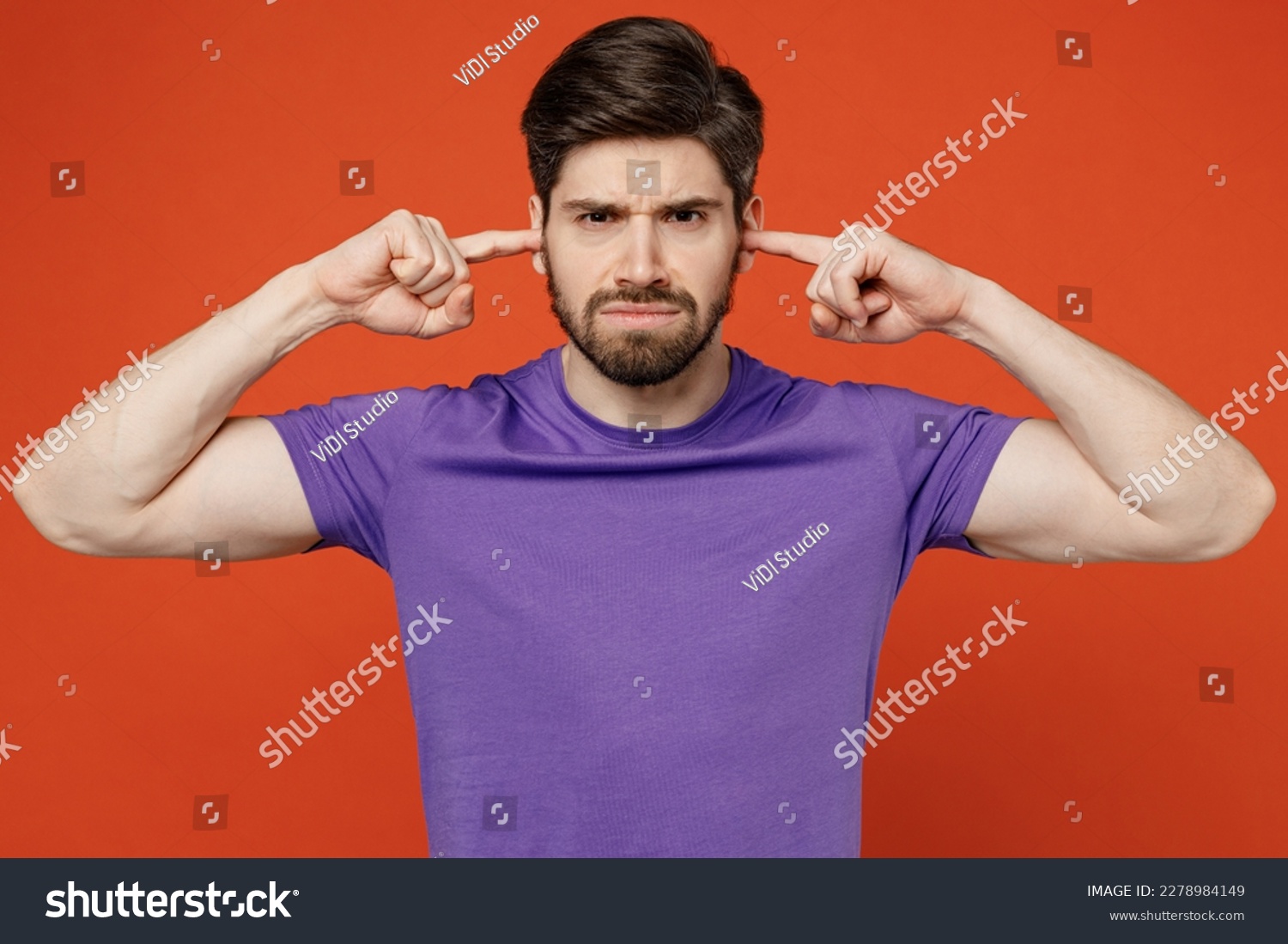 Young dissatisfied annoyed caucasian man wears casual basic purple t-shirt closed eyes cover ears with hands fingers do not want to listen scream isolated on plain orange background studio portrait #2278984149