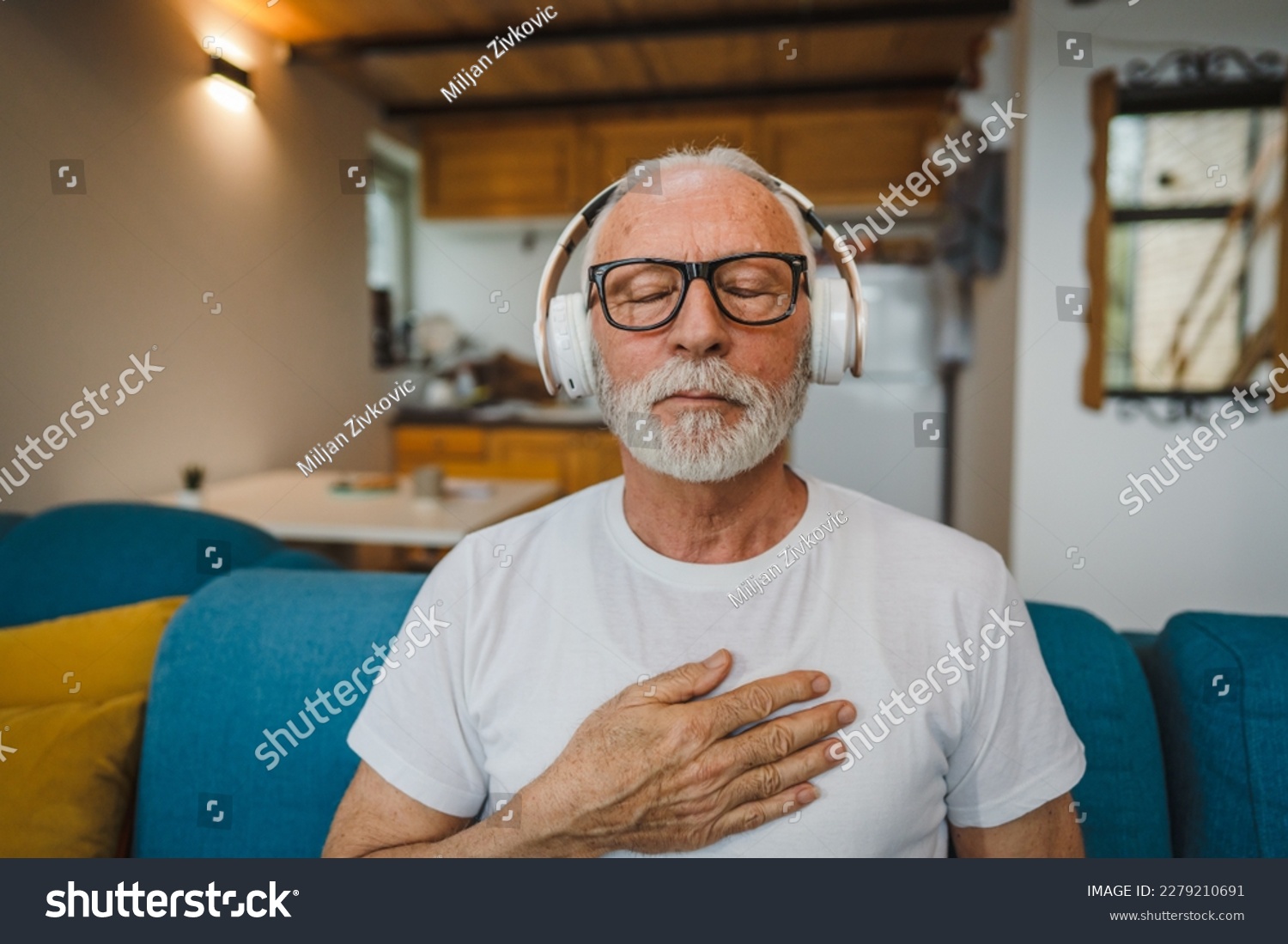 One man senior caucasian male eyes closed for guided training yoga or meditation while sitting at home with headphones self-care practice real people well-being inner peace and balance concept #2279210691