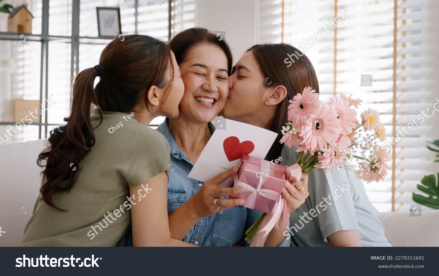 Mother day two grown up child cuddle hug give flower gift box red heart card to mature mum. Love kiss care mom asia middle age adult three people sitting at home sofa happy smile enjoy family time. #2279311691