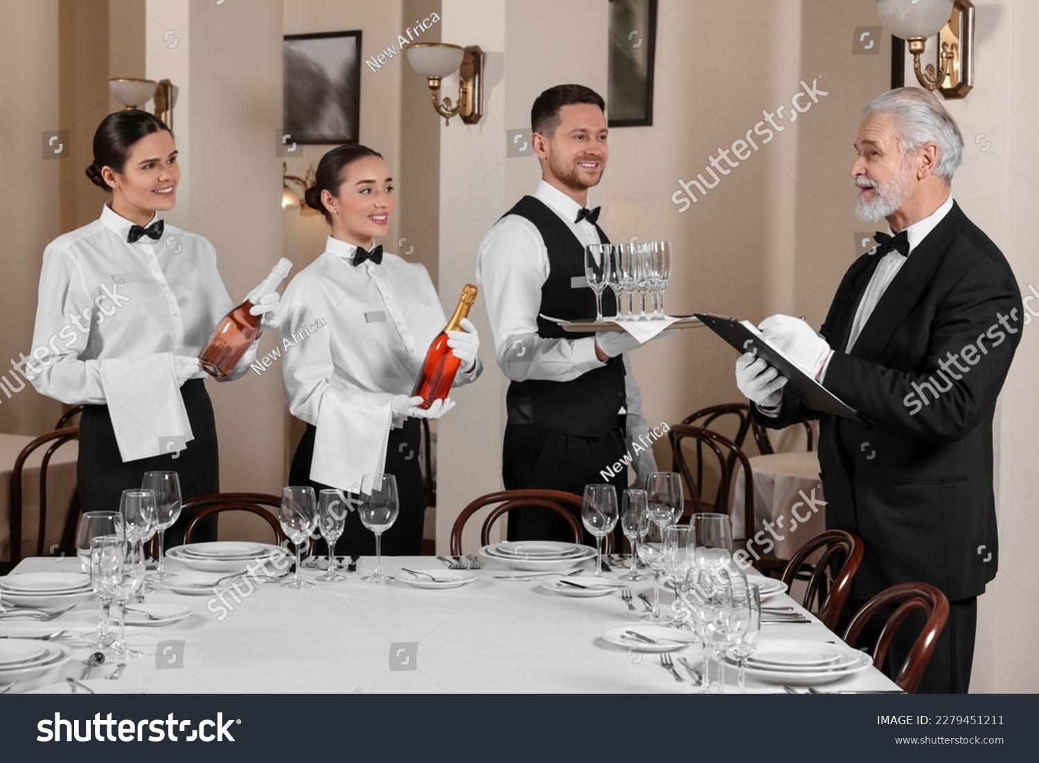 Senior man wearing formal suit teaching trainees in restaurant. Professional butler courses #2279451211
