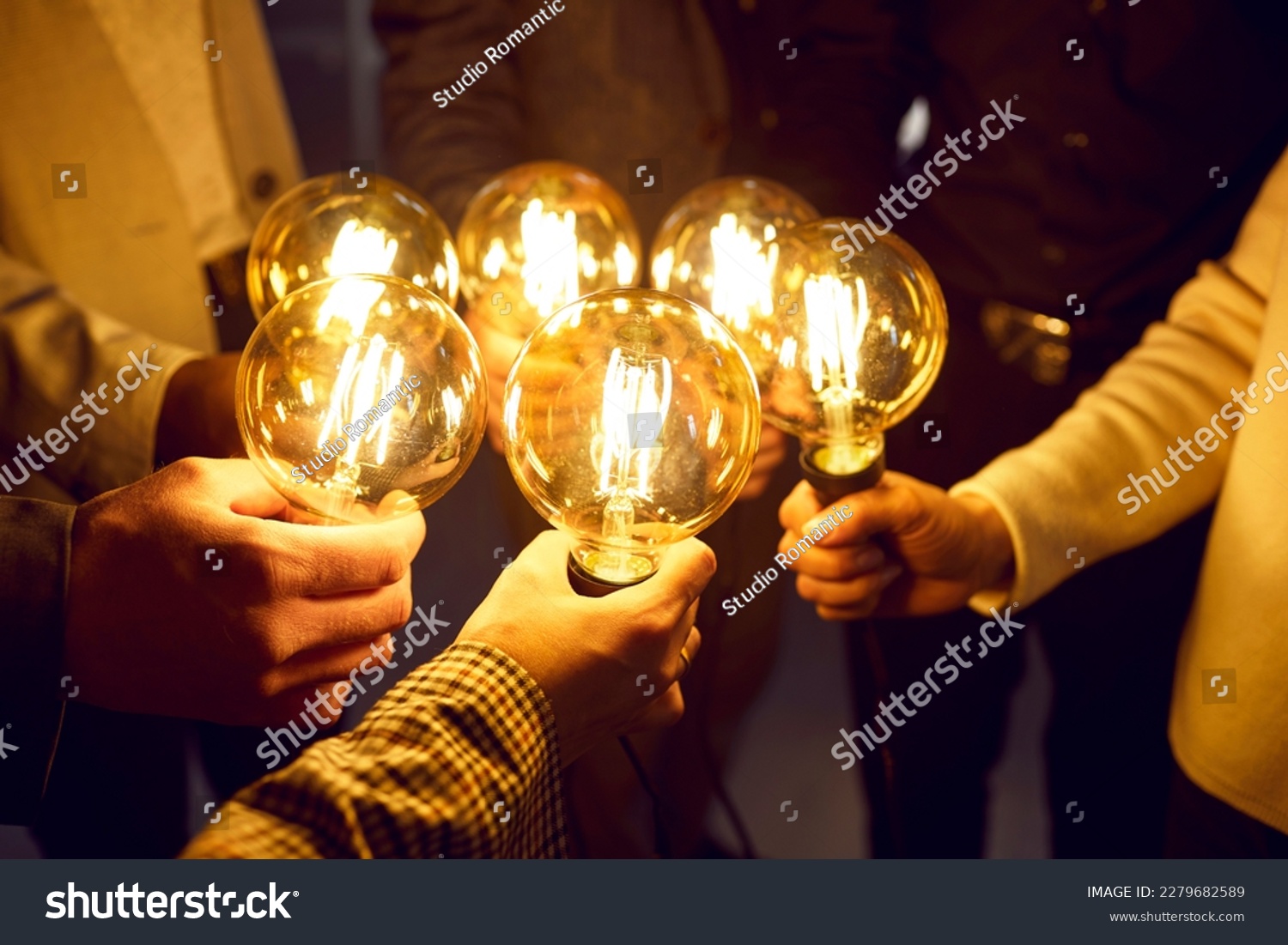 Business team sharing creative energy and developing new ideas. Group of people holding bright glowing electric Edison light bulbs as symbol of idea and innovation. Lightbulbs in human hands, close up #2279682589