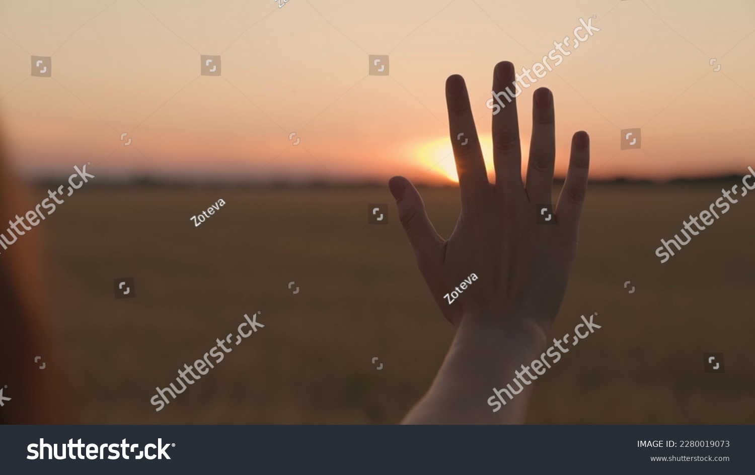 Happy girl stretches her hand to sunset. Sun between fingers of girls hands. Teenager with long hair holds out her hand at sunset. Childhood dream, express emotions in nature. Symbol of kind, warmth #2280019073