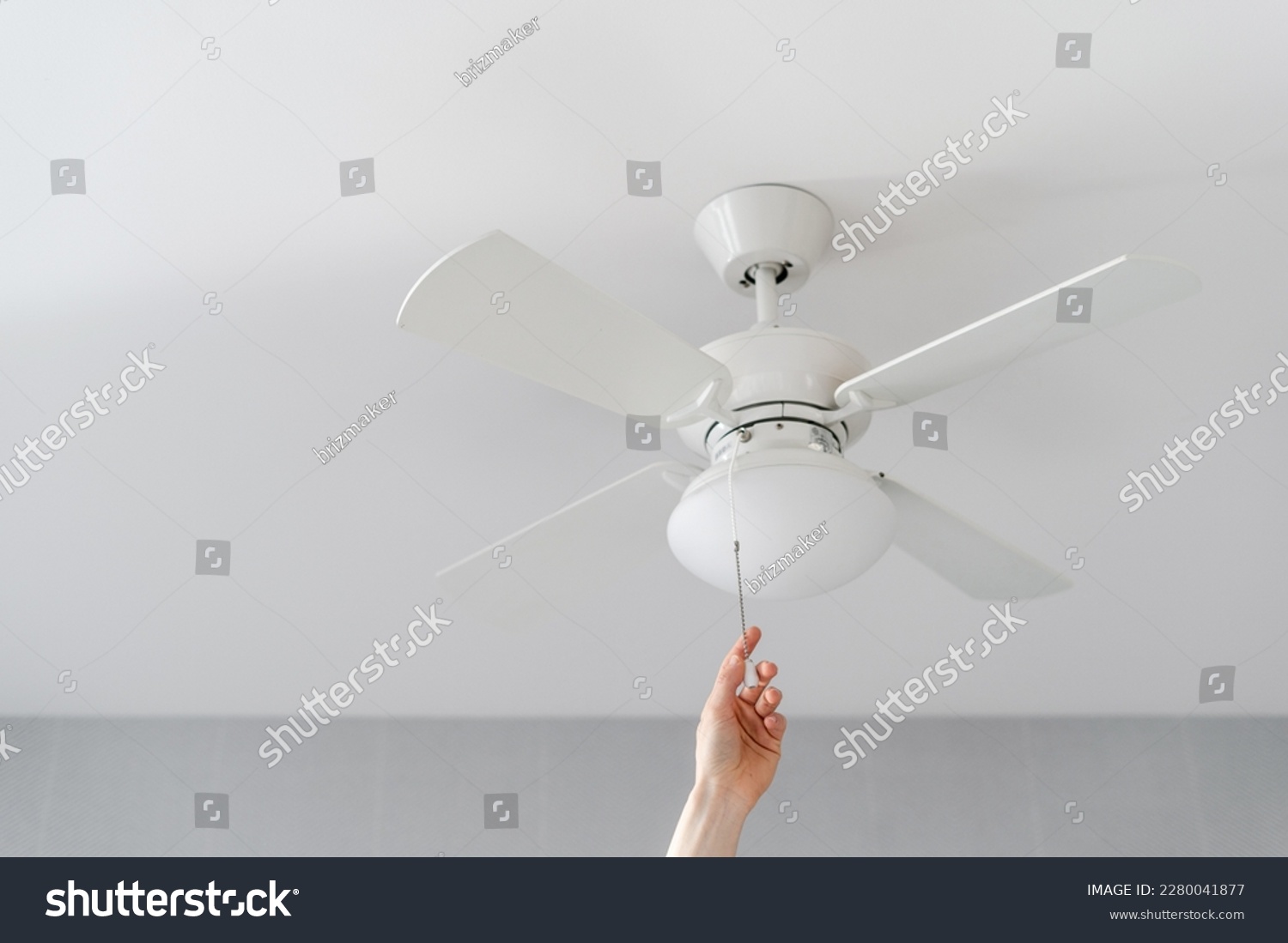 cropped shot of female hand pull switch of ceiling fan with lamp on white background with copy space, room cooling and ventilation concept #2280041877