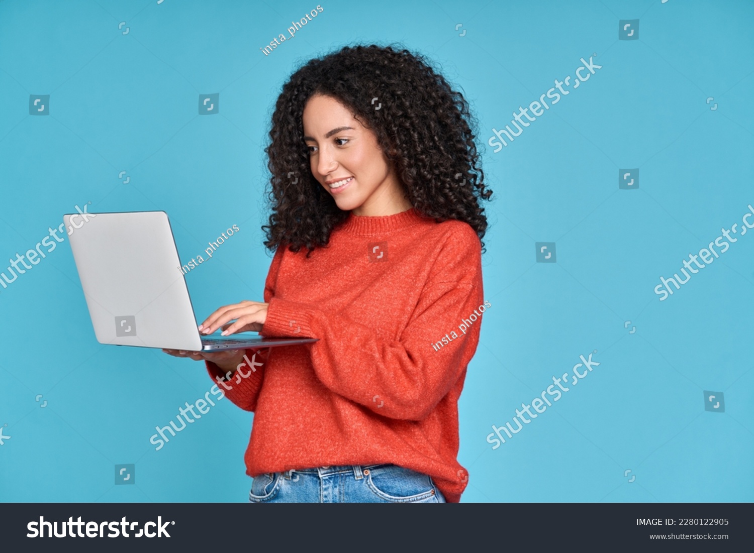 Young latin woman student using laptop device standing isolated on blue background. Smiling female model user holding computer, typing, surfing, searching job online or shopping website. #2280122905