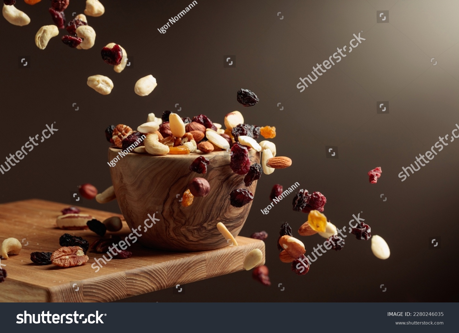 Flying dried fruits and nuts. The mix of nuts and dried berries are in a wooden bowl.  #2280246035