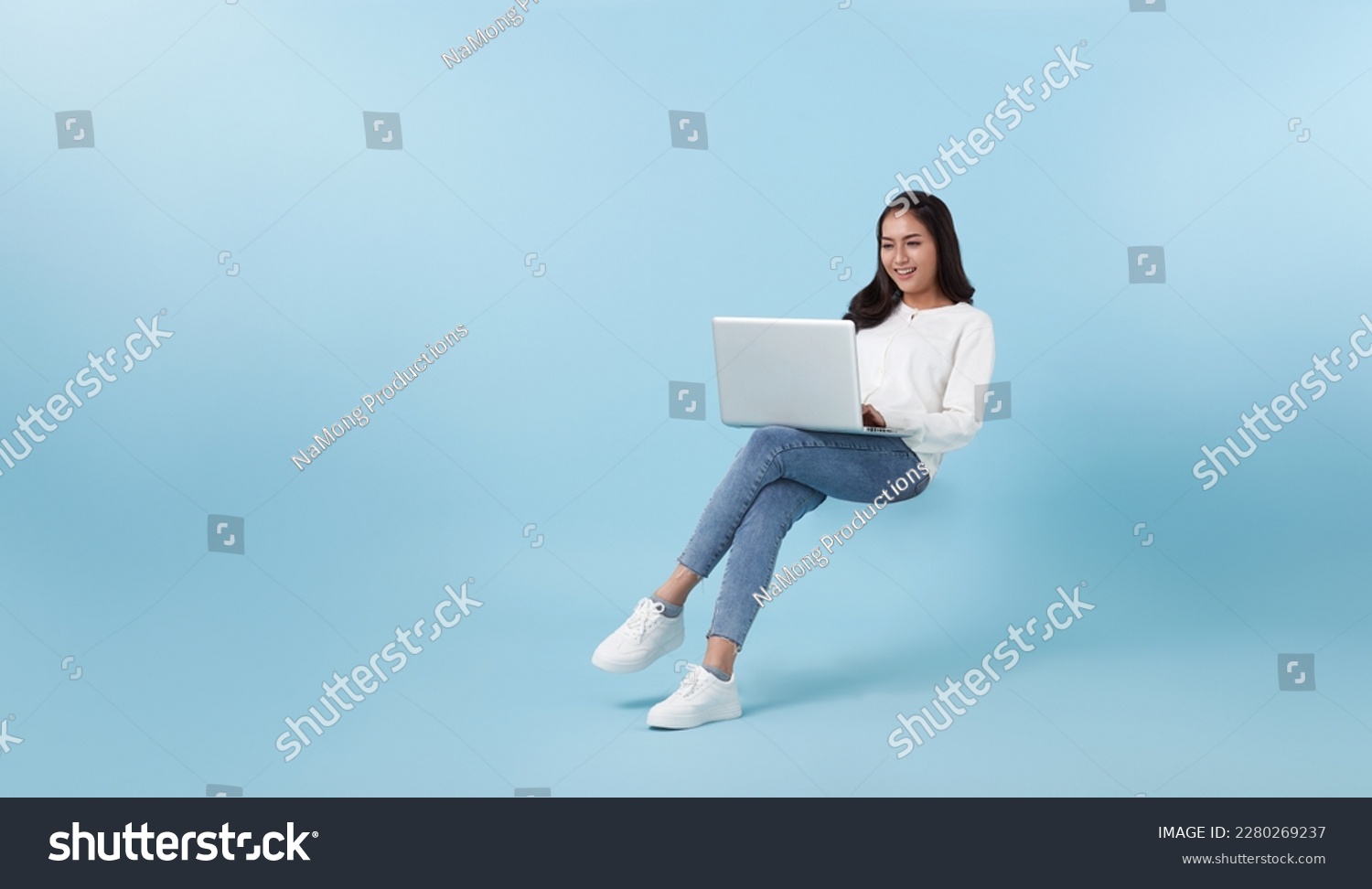 Young smiling Asian girl student floating in mid-air with using laptop isolated on blue studio copy space background. #2280269237