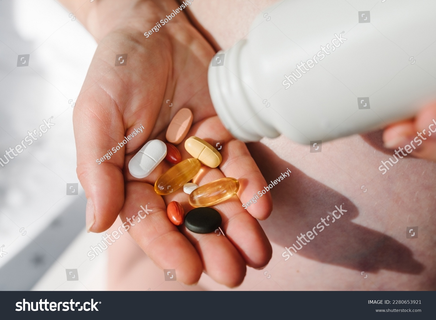 Closeup photo of supplements with a white bottle. Pregnant woman take omega 3, multivitamins, vitamins B, C, D, collagen tablets, probiotics, iron capsule. Girl hold vitamins daily. Top view. #2280653921