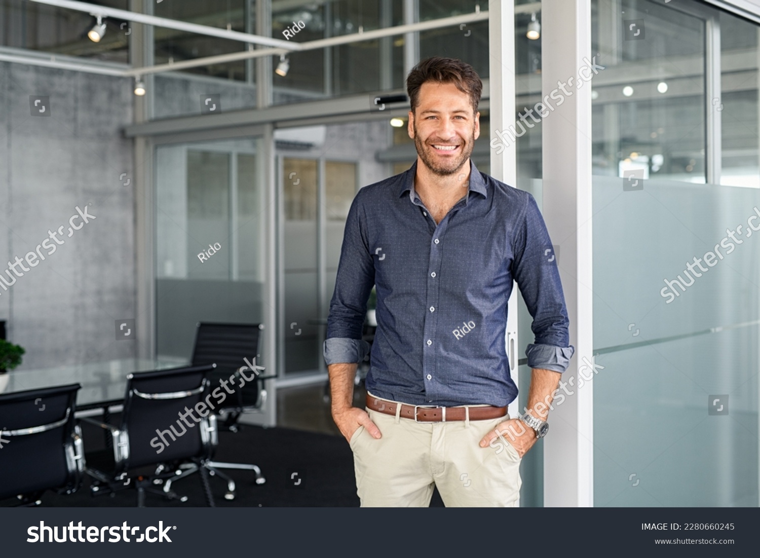 Portrait of mature successful man with hands in pocket standing outside office conference room. Businessman standing in office while looking at camera. Satisfied man in formalwear with copy space. #2280660245