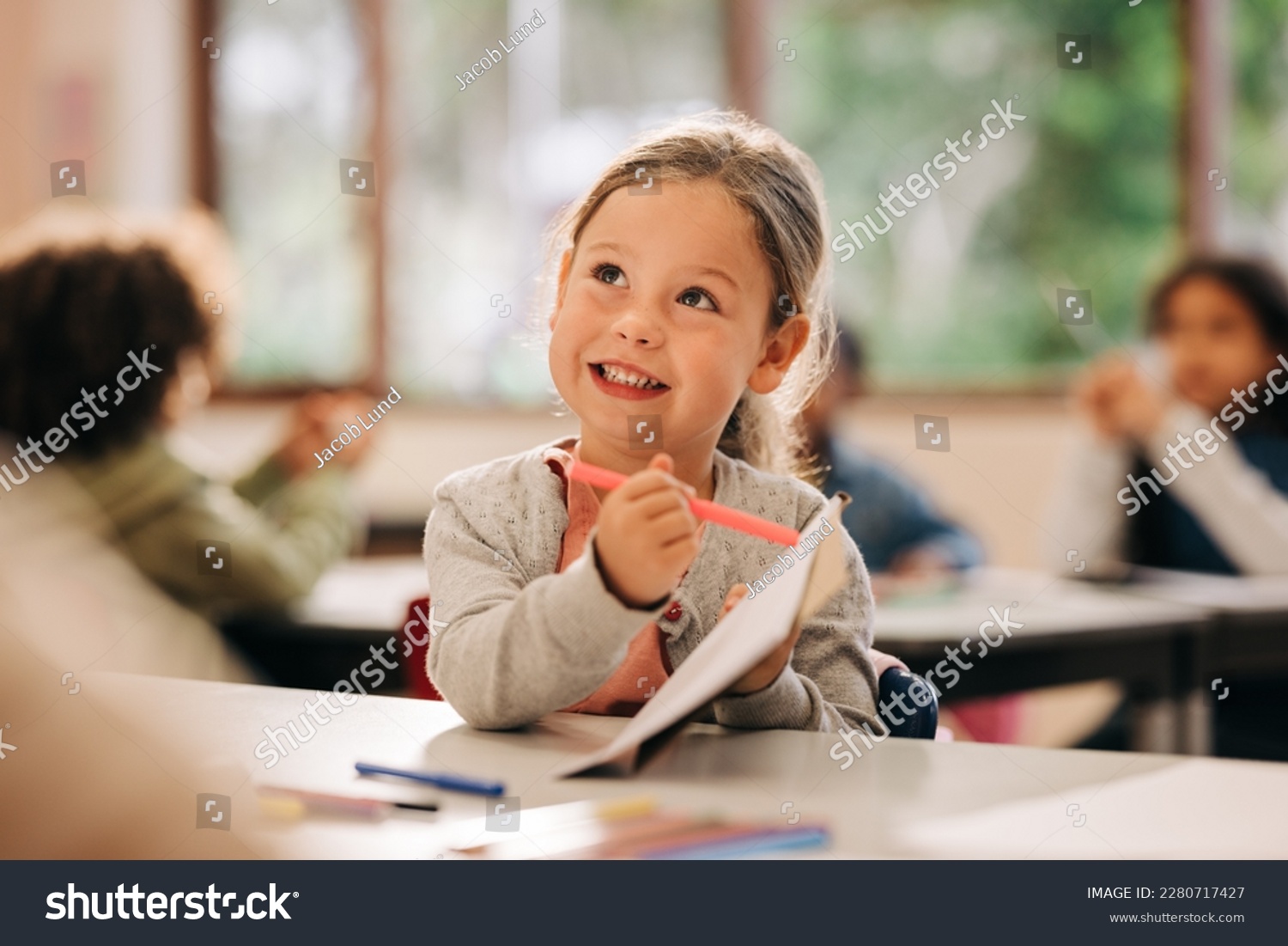 Happy little girl learning to draw with a colour pencil in an elementary art class. Primary school kid talking to her teacher as she receives quality education in a positive learning environment. #2280717427