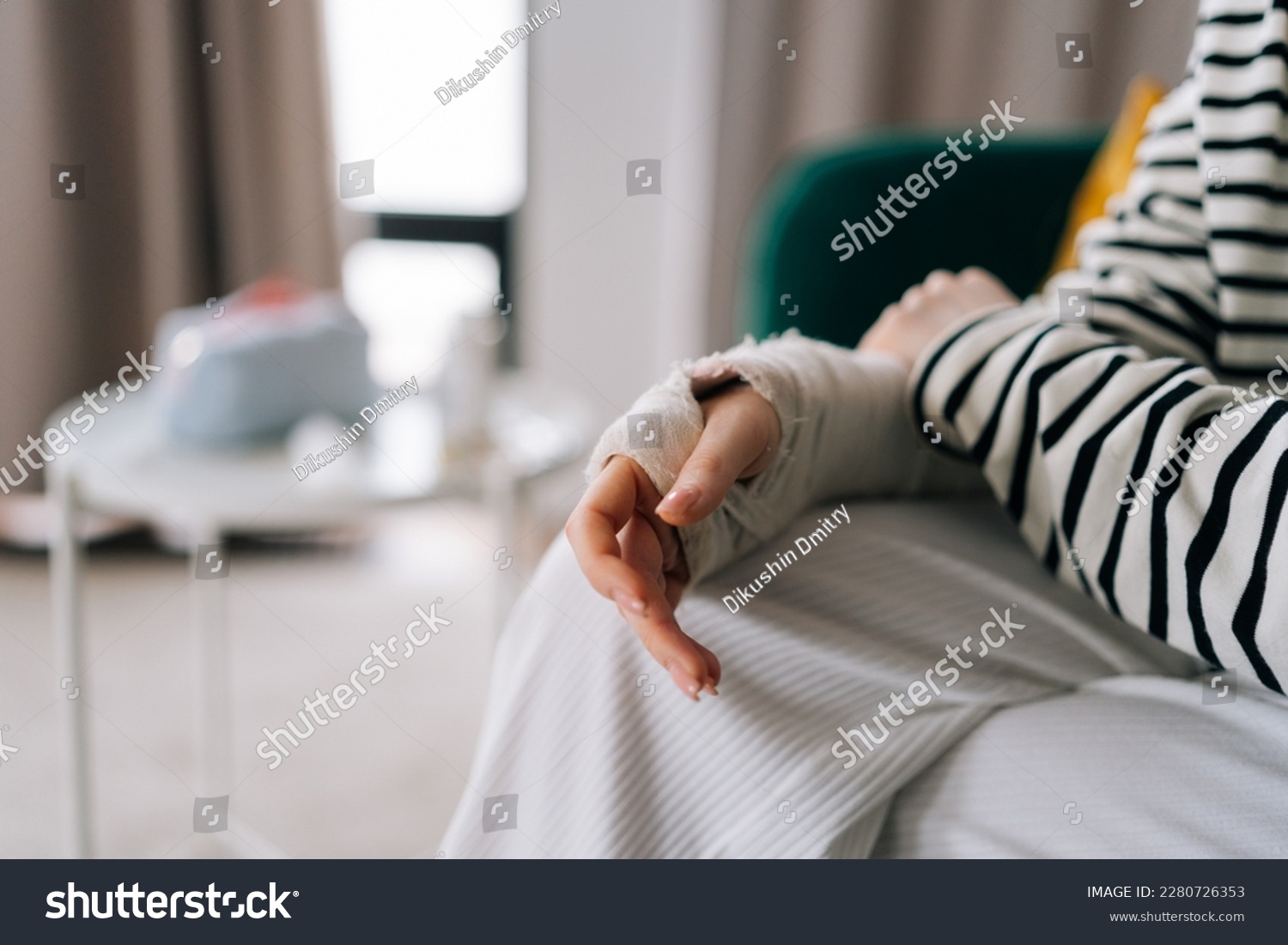 Detail cropped shot of suffering from pain unrecognizable young woman with broken hand wrapped in plaster bandage, gently massaging injured arm, sitting at home. Concept of insurance and healthcare. #2280726353