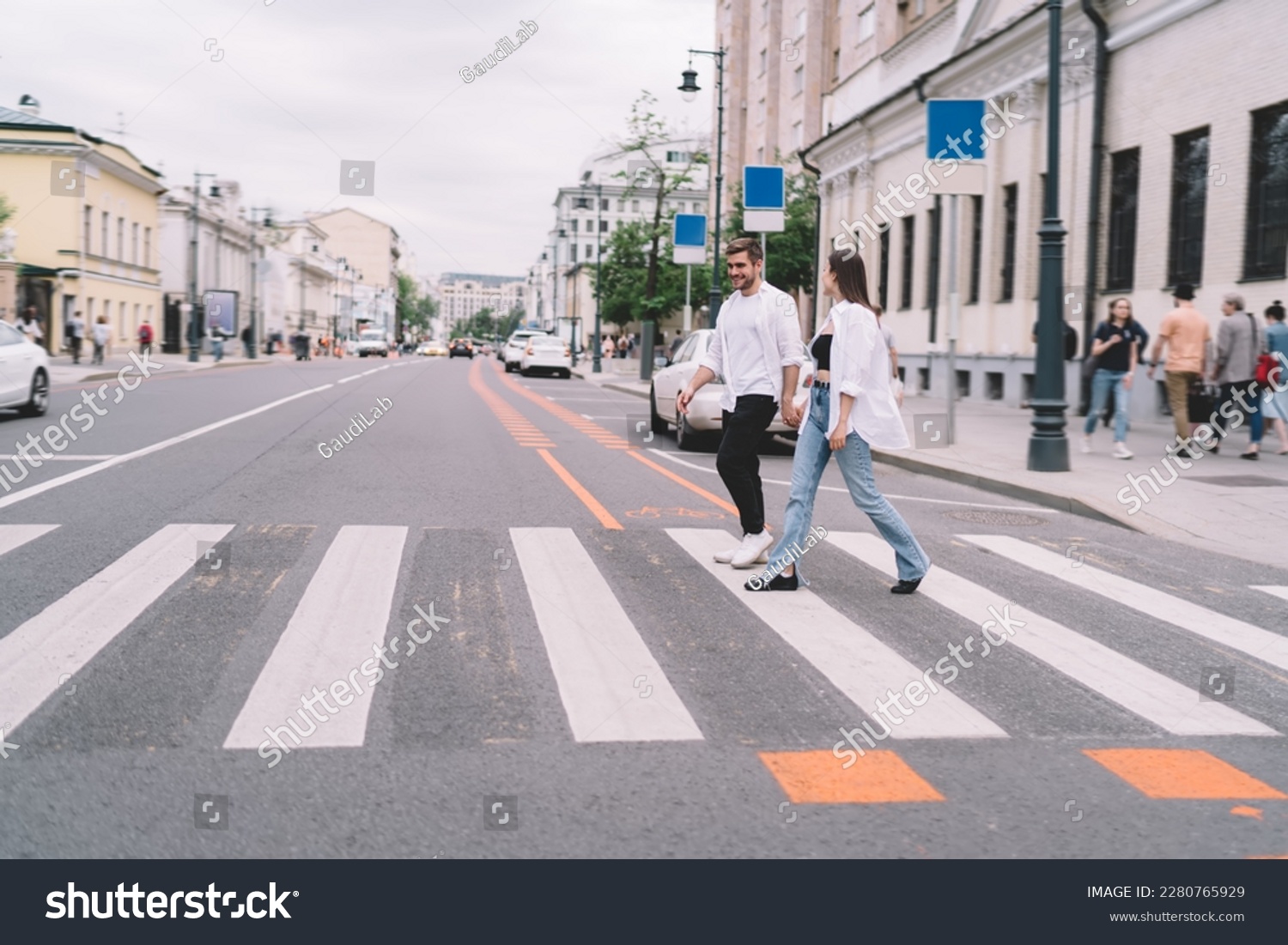 Full body of young man and woman in casual clothes holding hands while crossing street on crosswalk during date in city #2280765929