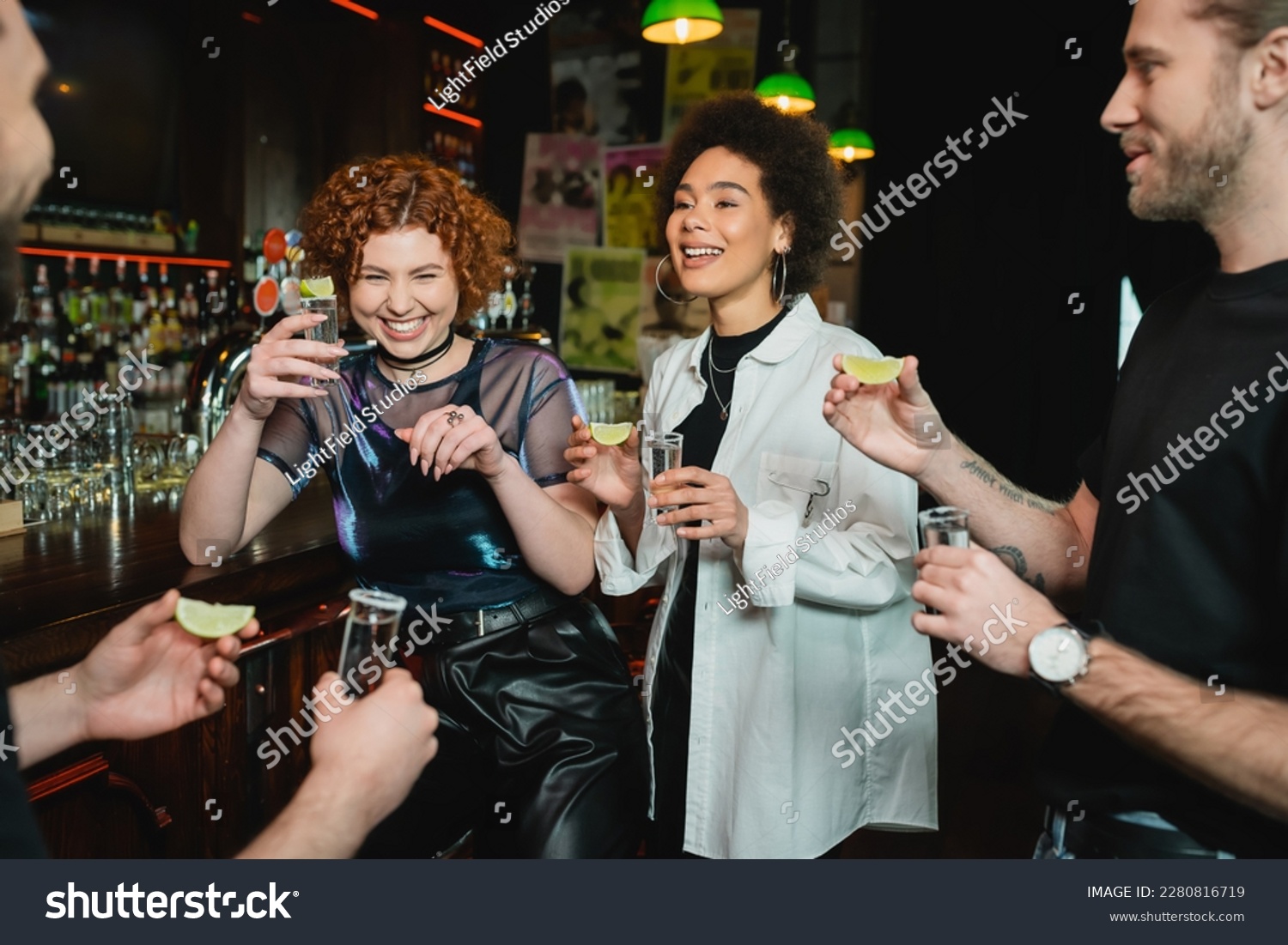 Cheerful multiethnic people having fun and holding tequila shots in bar #2280816719