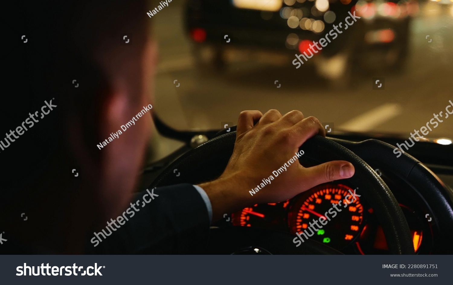 Man driving car fast in night city street with traffic. Road trip, speeding, driver concept. Commuter, male taxi cab driver. Interior back view of male hand on steering wheel in car. Close up #2280891751