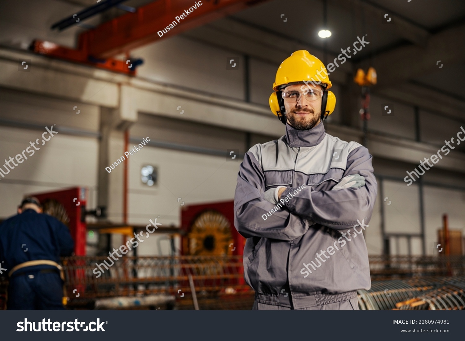 A heavy industry and metallurgy worker in protective uniform is proudly standing in facility and smiling at the camera. #2280974981