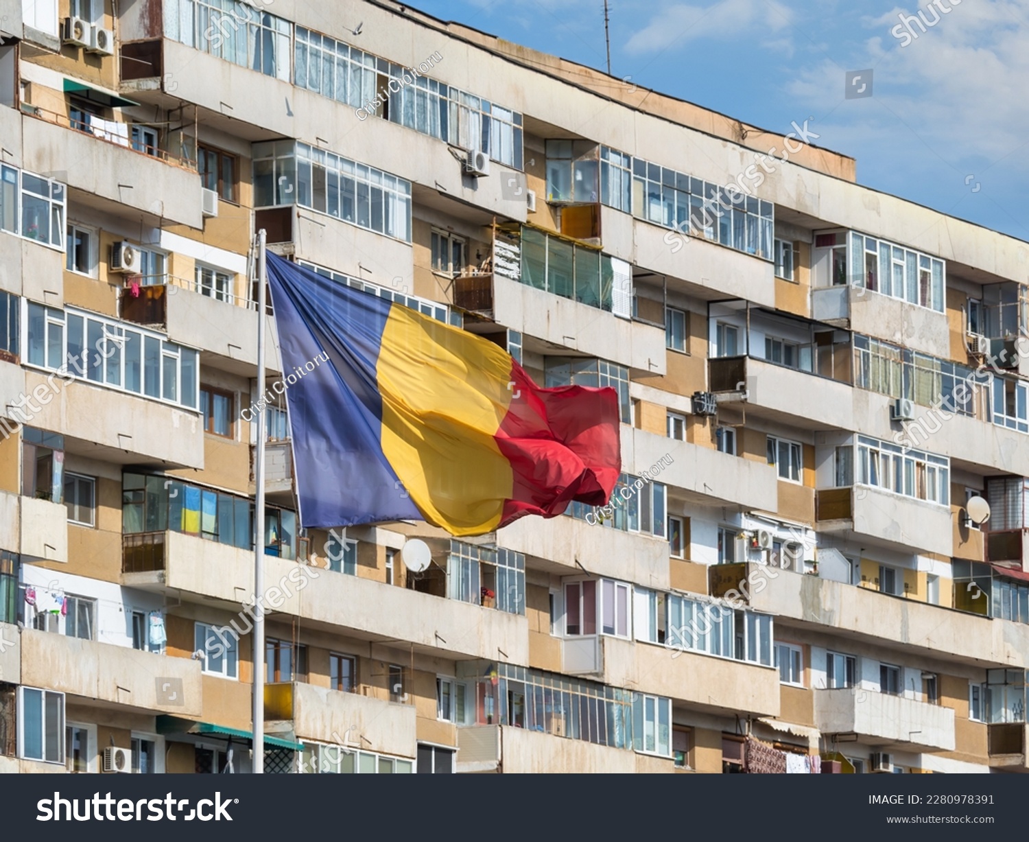 Romanian national flag in the wind and a worn out communist apartment building in the background, in Bucharest Romania. #2280978391