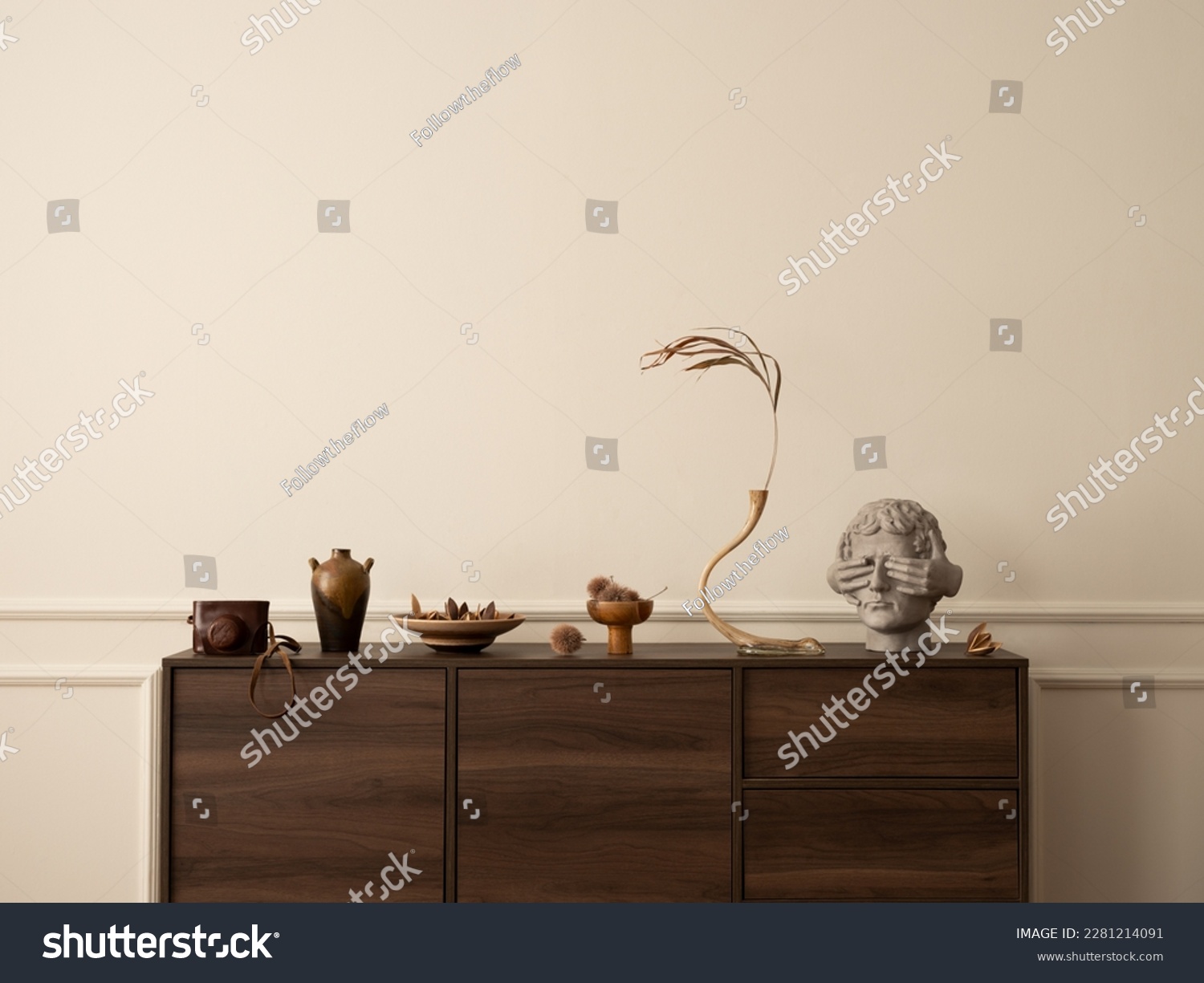 Aesthetic composition of living room interior with wooden sideboard, glass vase with dried flowers, modern sculpture, nuts, wall with stucco and personal accessories. Home decor. Template. #2281214091