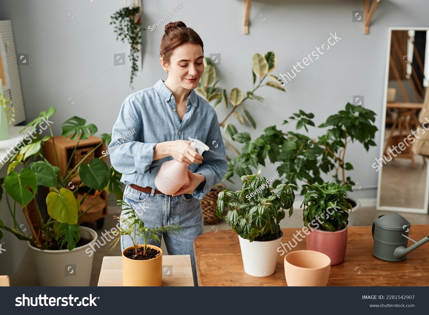 Portrait of smiling young woman watering plants indoors and caring for home greenery, copy space #2281542907
