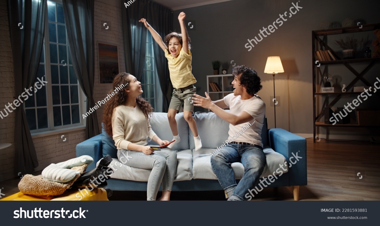 Excited naughty, noisy Asian child jumping around mom and dad on sofa, shouting, annoyed. hyperactive little son jumping on sofa and drawing attention. #2281593881