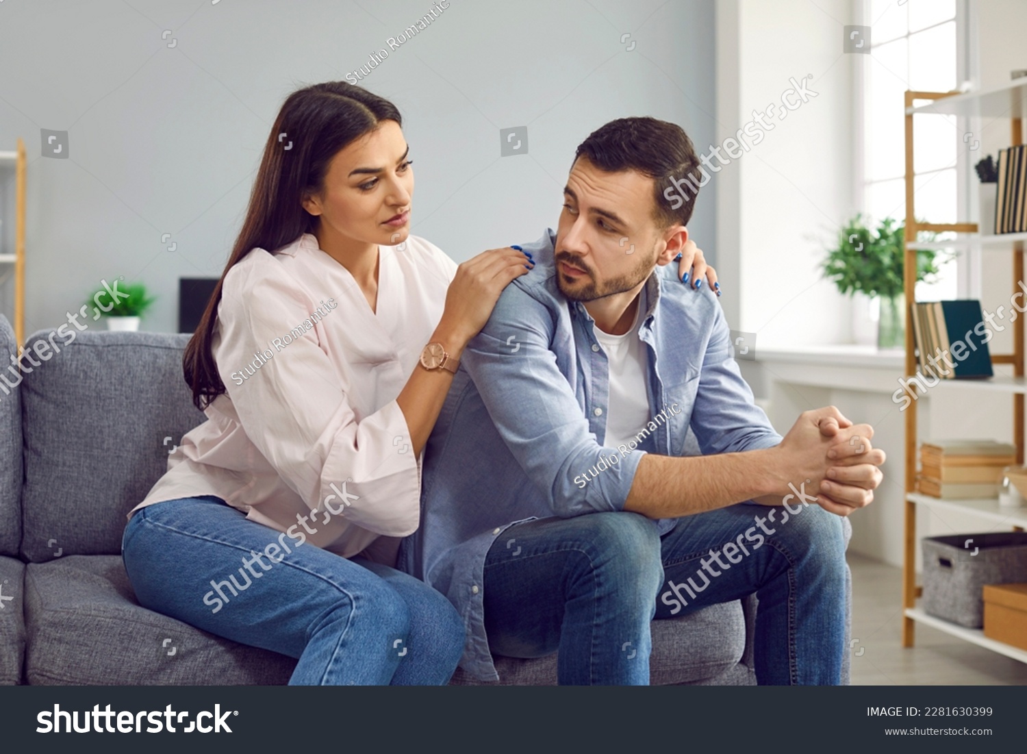 Attractive wife hugging husband from back to comfort or apologize. Young woman hugging upset man, expressing understanding, saying sorry, showing support. Couple sitting on sofa at home #2281630399