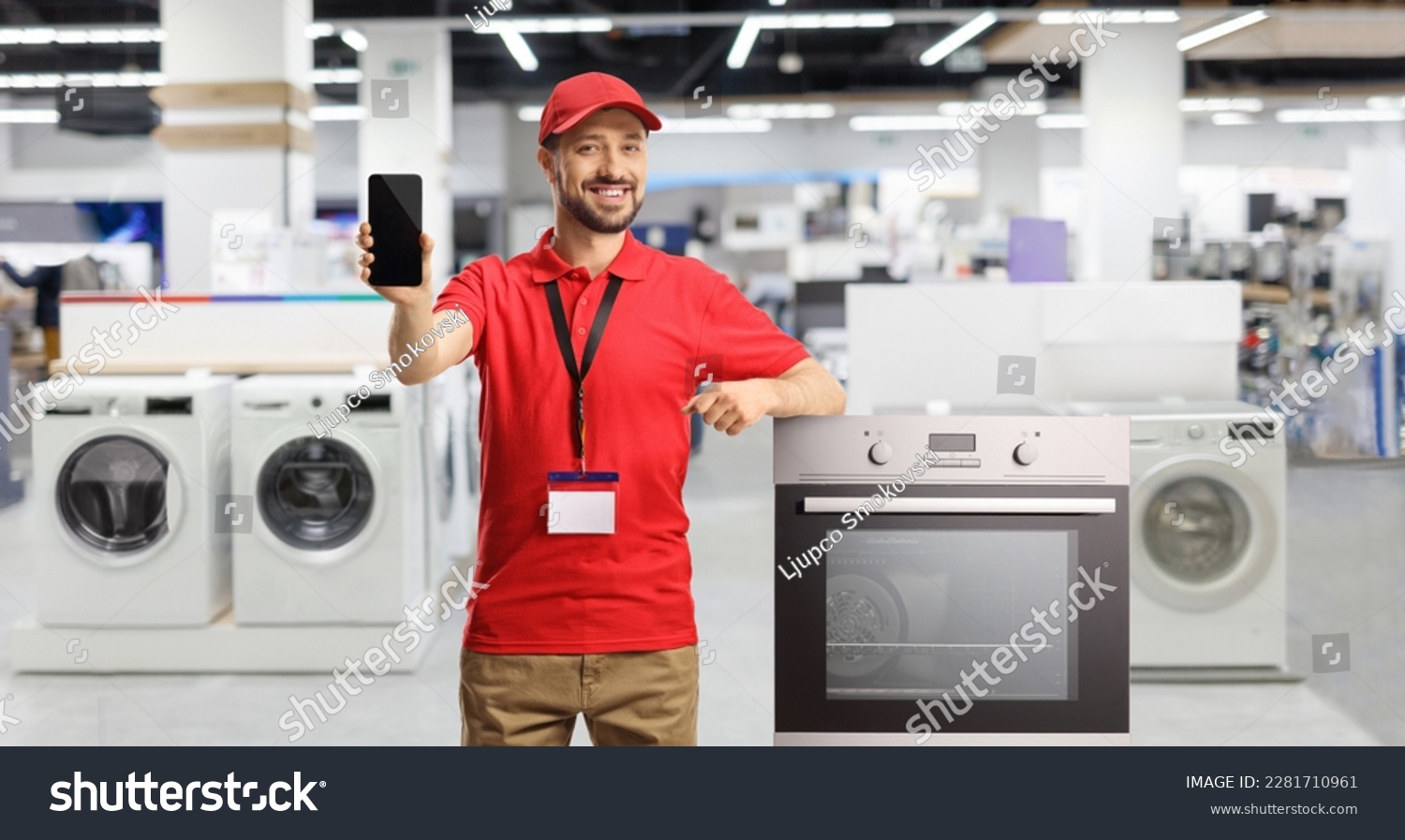 Male shop assistant with an oven smiling and showing a smartphone inside a store #2281710961