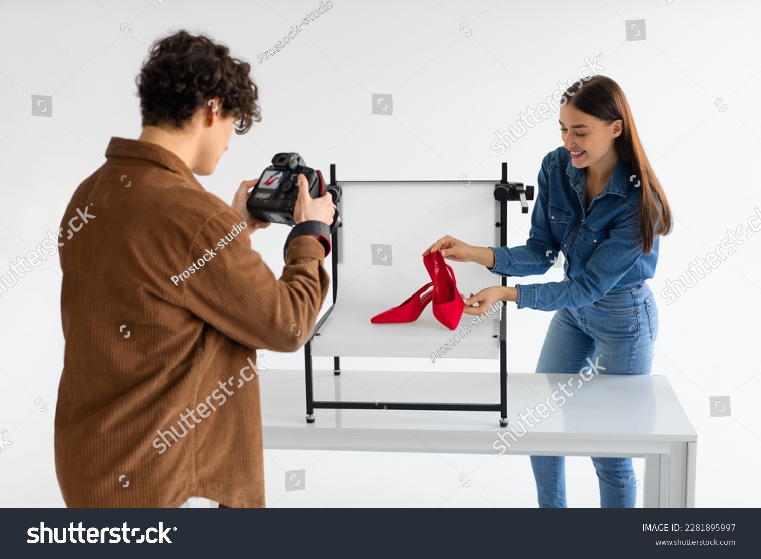 Professional male photographer and his female assistant doing content photoshoot for shoes, woman styling and helping while working in team in photostudio #2281895997