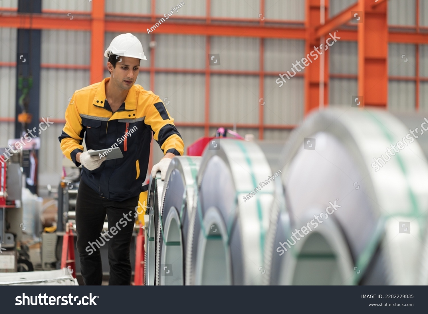 Metalwork manufacturing, warehouse of raw materials. Male factory worker inspecting quality rolls of metal sheet in factory during manufacturing process, wearing safety uniform, use digital tablet #2282229835
