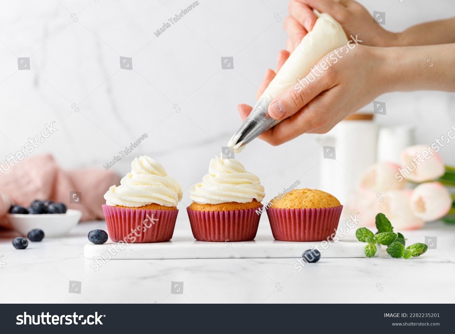 Making, decorating cupcakes, muffins with cream, blueberries and green mint leaves. Delicious homemade dessert. Pastry Process. Copy space. Pastry bag. #2282235201