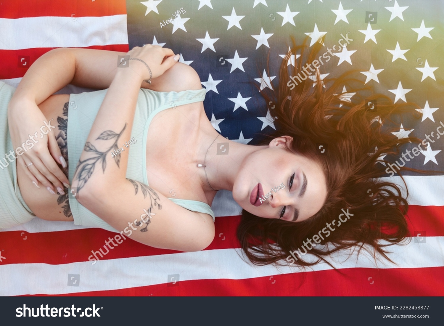 Top view of jewish pretty lady model lying down on american flag, dreaming, closed eyes. Young cute brunette woman with tattoo at flag of USA background. American dream concept. Copy ad text space #2282458877